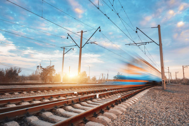 High speed blue passenger train in motion on railroad at sunset. Blurred commuter train. Railway station against colorful sky. Railroad travel, railway tourism. Rural industrial landscape. Vintage tren de pasajeros azul de alta velocidad en movimiento en el ferrocarril al atardecer. tren de cercanías borroso. estación de ferrocarril contra el cielo colorido. viajes ferroviarios, turismo ferroviario. paisaje industrial rural. vintage