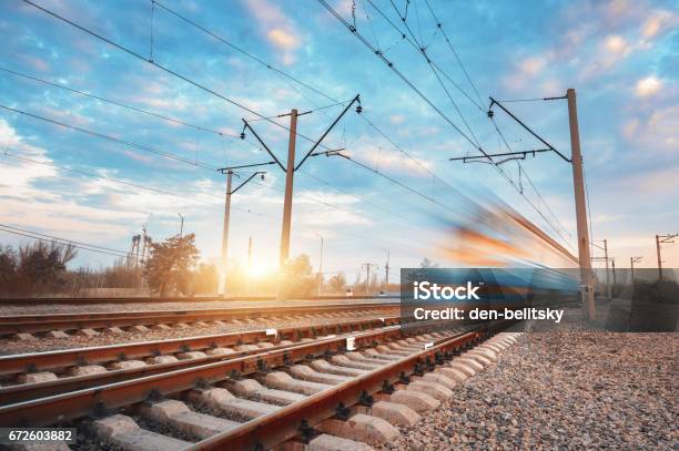 Photo libre de droit de Train De Voyageurs Bleu À Grande Vitesse En Mouvement Sur Le Chemin De Fer Au Coucher Du Soleil Train De Banlieue Brouillé Station De Chemin De Fer Contre Le Ciel Coloré Voyages Ferroviaires Tourisme Ferroviaire Paysage Industriel Rural Année banque d'images et plus d'images libres de droit de Transport ferroviaire