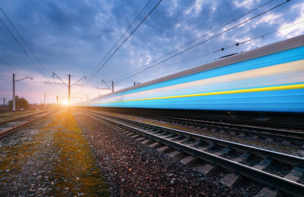 istock High speed blue passenger train in motion on railroad track at sunset. Blurred modern train. Railway station against dramatic cloudy sky. Railroad travel, railway tourism. Rural industrial landscape 672603892