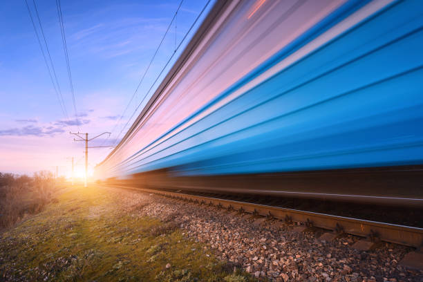 High speed blue passenger train in motion on railroad at sunset. Blurred modern commuter train. Railway station and colorful sky. Railroad travel, railway tourism. Rural industrial landscape in dusk. tren de pasajeros azul de alta velocidad en movimiento en el ferrocarril al atardecer. tren de cercanías moderno borroso. estación de ferrocarril y cielo colorido. viajes ferroviarios, turismo ferroviario. paisaje industrial rural al atardecer.