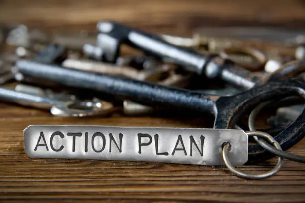 Photo of key bunch on wooden board and tag with letters imprinted on clean metal surface; concept of ACTION PLAN