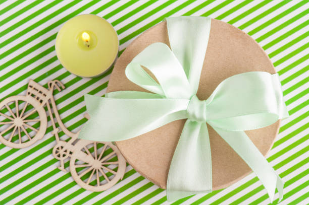 Lit candle and gift box with green ribbon on a striped background. Top view