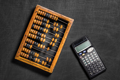 Old wooden scratched vintage decimal abacus and calculator on a black desktop from chalkboard with blank for inscription for the background. Top view. Flat lay. Mockup