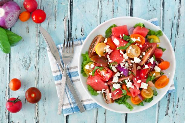 Watermelon and tomato salad with feta, overhead on blue wood Watermelon and mixed tomato salad with feta cheese, overhead scene on rustic blue wood cheese goat cheese gourmet food stock pictures, royalty-free photos & images