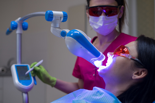 Smiling Female Dentist Adjusting Light Before Taking In Patients With Her Assistants