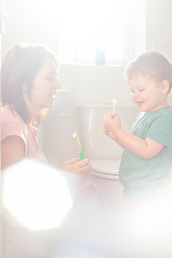A mother teaches her young toddler how to brush his teeth.