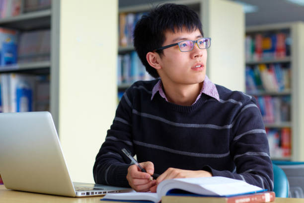 istock One male asian college student study in the library with laptop on table 672688916