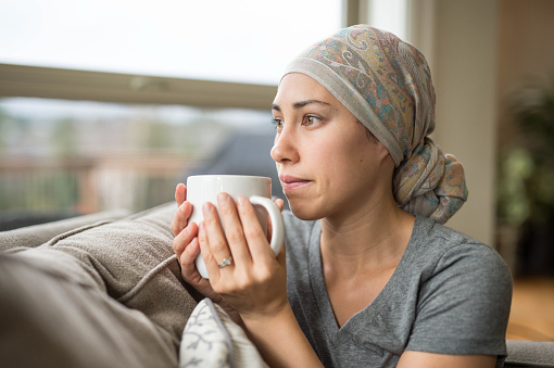 Ethnic young woman with cancer drinking cup of tea on couch