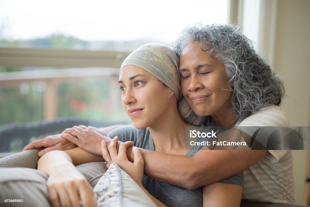 Hawaiian woman in 50s embracing her mid-20s daughter on couch who is fighting cancer Cancer - Illness Stock Photo