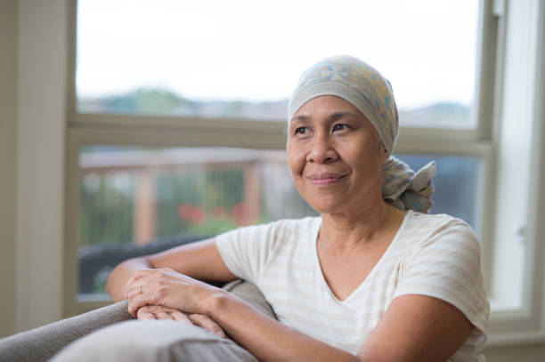 mature ethnic woman with cancer wearing headwrap on couch - cancer chemotherapy drug patient women imagens e fotografias de stock
