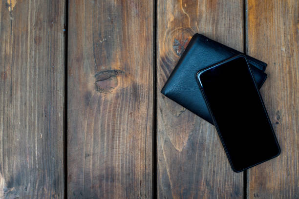 Black smartphone and leather wallet placed on wood table