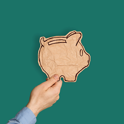 Man holding paper cut in form of a piggy bank in front of a coloured background