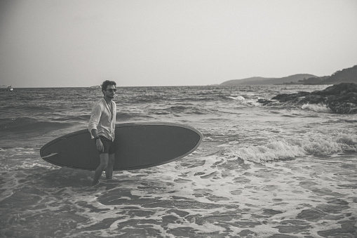 One man, surfer man on the beach, holding his surfboard, black and white.