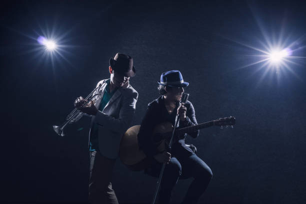 Musician Duo band playing a trumpet and singing a song and playing the guitar on black background with spot light and lens flare, vintage cool tone color, musical concept Musician Duo band playing a trumpet and singing a song and playing the guitar on black background with spot light and lens flare, vintage cool tone color, musical concept hair band stock pictures, royalty-free photos & images