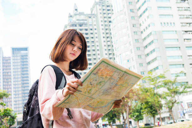 istock Cheerful woman wanderer with trendy look searching direction on location map 672734348