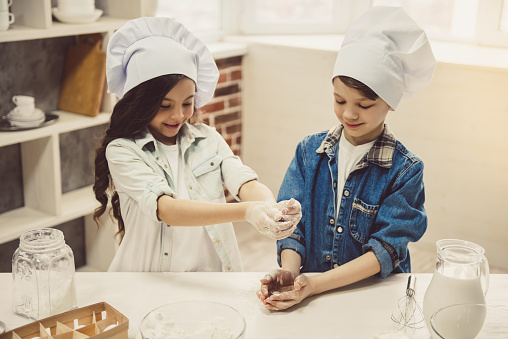 Cute children in chef hats are preparing dough and smiling while baking in the kitchen