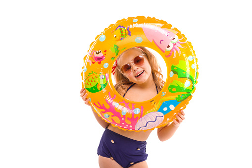 Isolated on white, pretty cute caucasian blonde girl in red striped bikini, blue bottoms, sunglasses and pink flower wreath hold colorful rubber ring near her face, close, laughing