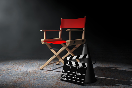 Cinema Industry Concept. Red Director Chair, Movie Clapper and Megaphone in the volumetric light on a black background. 3d Rendering.