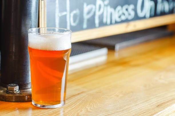 Nonic pint glass full of pale ale standing on a bar counter