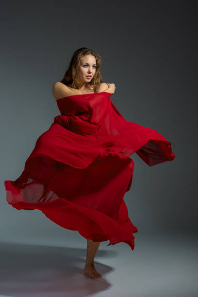istock Young beautiful dancer in red dress posing on a dark gray studio background 672771022