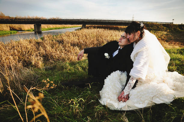 pareja de bodas en el campo sentado sobre hierba - silhouette kissing park sunset fotografías e imágenes de stock