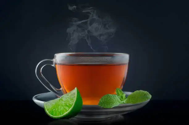 Cup tea with mint and lime on a black background.