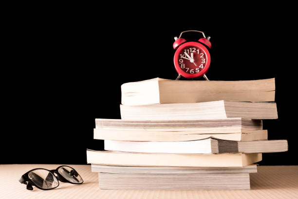 istock Stack of books with eyeglasses and clock on wooden table, Black background 672788768