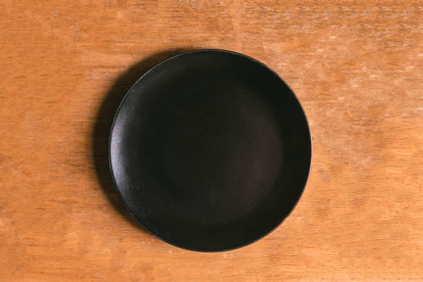 istock Top view of empty black plate on wooden table 672789472
