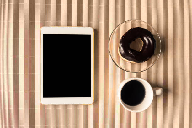 istock Top view of tablet with coffee cup and donut on table. 672789528