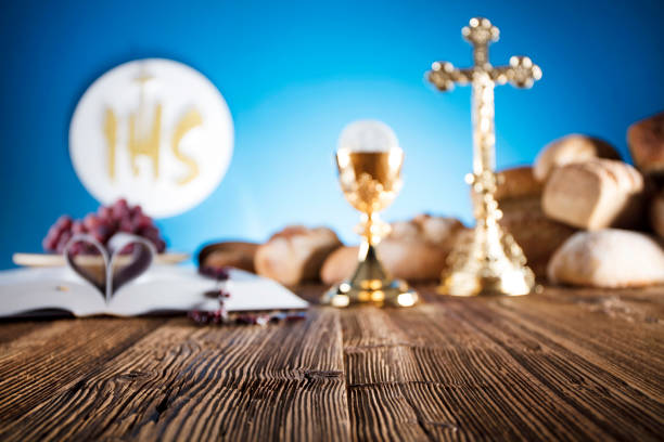 istock First Holy communion. Catholic theme. Crucifix, chalice, bible, bread on rustic wooden table and blue background. 672792712