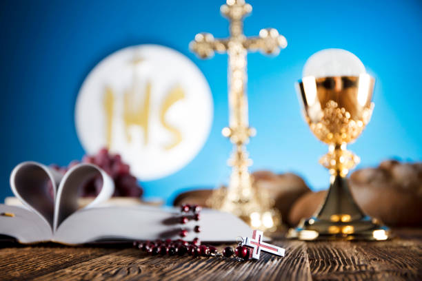 istock First Holy communion. Catholic theme. Crucifix, chalice, bible, bread on rustic wooden table and blue background. 672792916