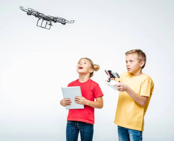 Happy kids using digital tablet and hexacopter drone isolated on white