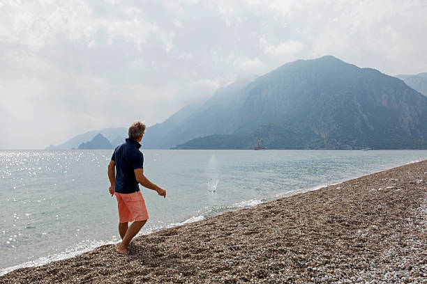 istock Man skips rocks on Mediterranean. Mountain behind 672817977