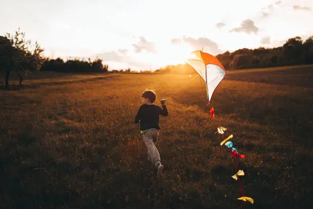 Little boy is running a kite, on a beautiful sunny day he is spending outdoors in nature