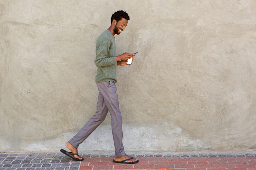 Full body portrait of handsome black man walking with smart phone and coffee cup
