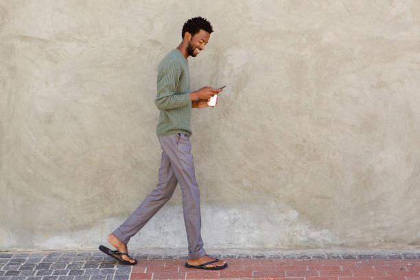 full body portrait of handsome man walking with smart phone - wall profile imagens e fotografias de stock