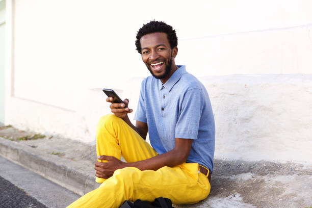 istock laughing man holding smart phone sitting by wall 672846414