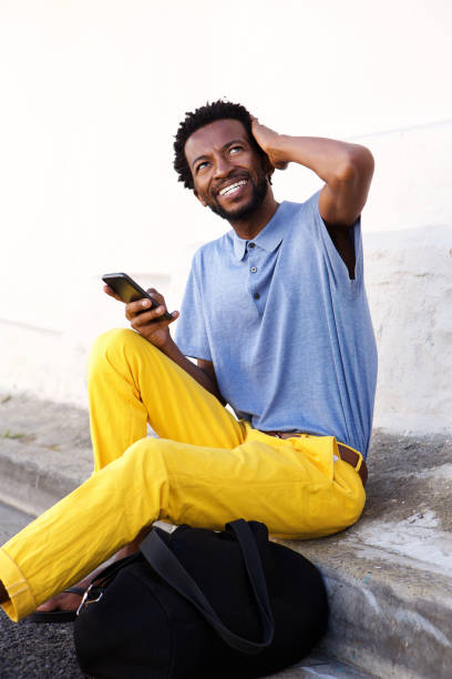 istock smiling man sitting and holding smart phone with bag 672846468
