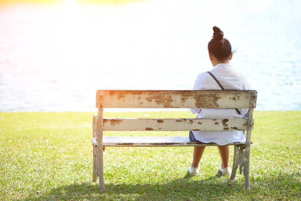 istock Woman sitting alone on a bench in the park 672861366