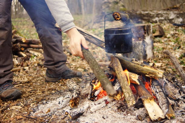 istock Tourist kettle on camp fire with tent on background. hand with stick about fire.a 672867214