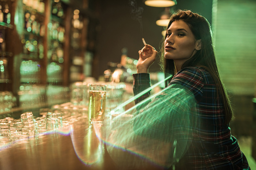 Young woman sitting alone in a bar and smoking a cigarette.