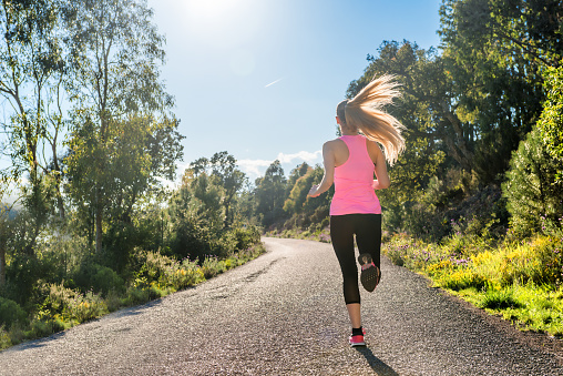 Horizontal color rear view image of beautiful young woman running outdoors. Happy sportswoman enjoying relaxation exercise in beautiful environment.