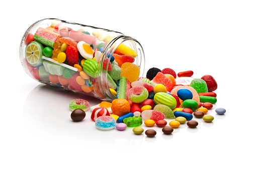 Three-quarter front view of an open candy jar filled with multi colored candies and jelly beans lying down on white background. Some candies are spilled out of the jar directly on the background. DSRL studio photo taken with Canon EOS 5D Mk II and Canon EF 100mm f/2.8L Macro IS USM