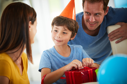 Shot of a little boy opening his birthday presents surrounded by his family