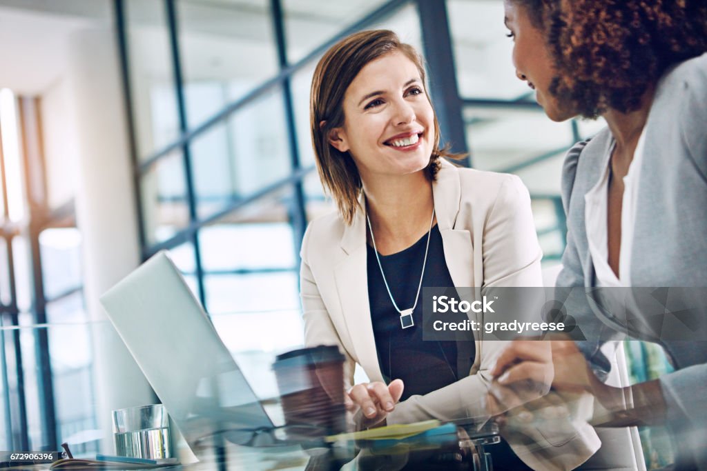 Keeping productivity levels up with effective collaboration Shot of two young businesswomen using a laptop together at work Discussion Stock Photo