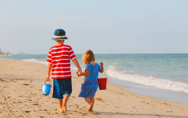istock little boy and girl walking on beach 672909824