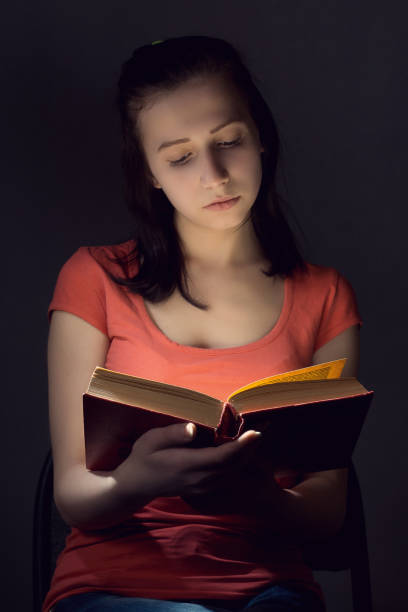 istock Cute girl reading a book in the dark 672909912