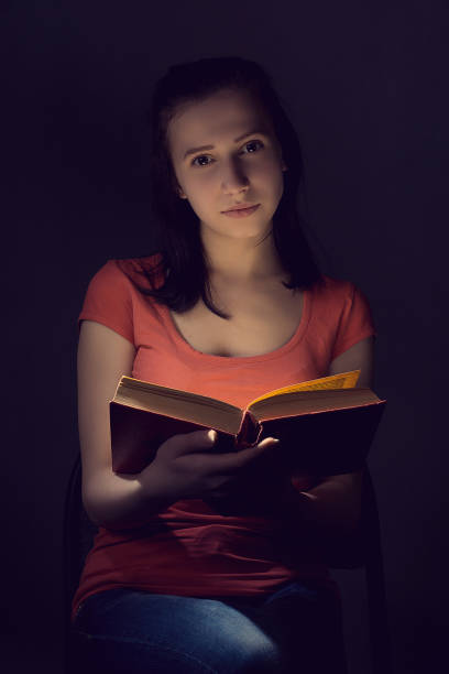 istock Cute girl reading a book in the dark 672909914