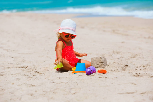 istock cute little girl play with sand on beach 672910084