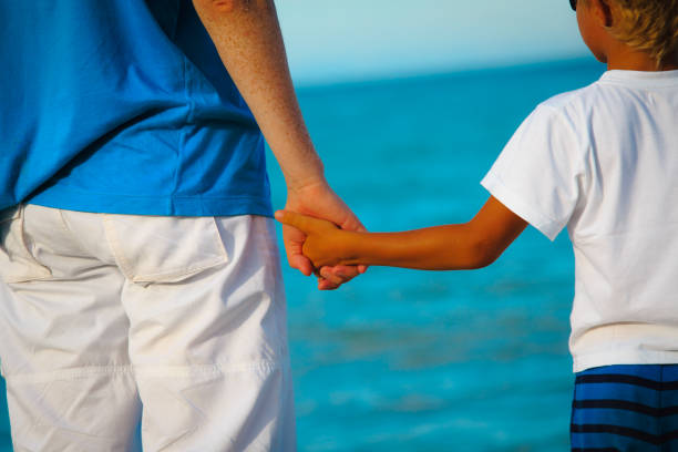 istock father and little son holding hands at beach 672914522